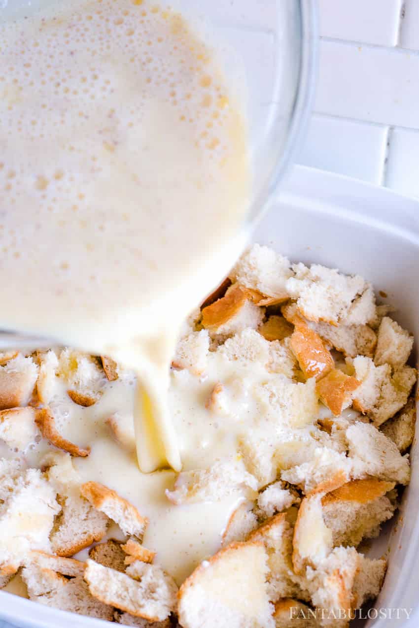 Close-up image of egg custard batter pouring out of mixing bowl on to top of bread