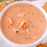 Lobster bisque in small bowl with crackers on a plate underneath.