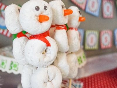 White powdered donuts on a stick with candy to make snowmen