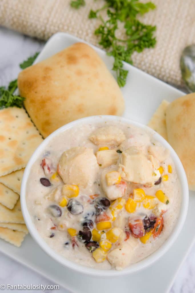 White chicken chili in white bowl with rolls & parsley surrounding