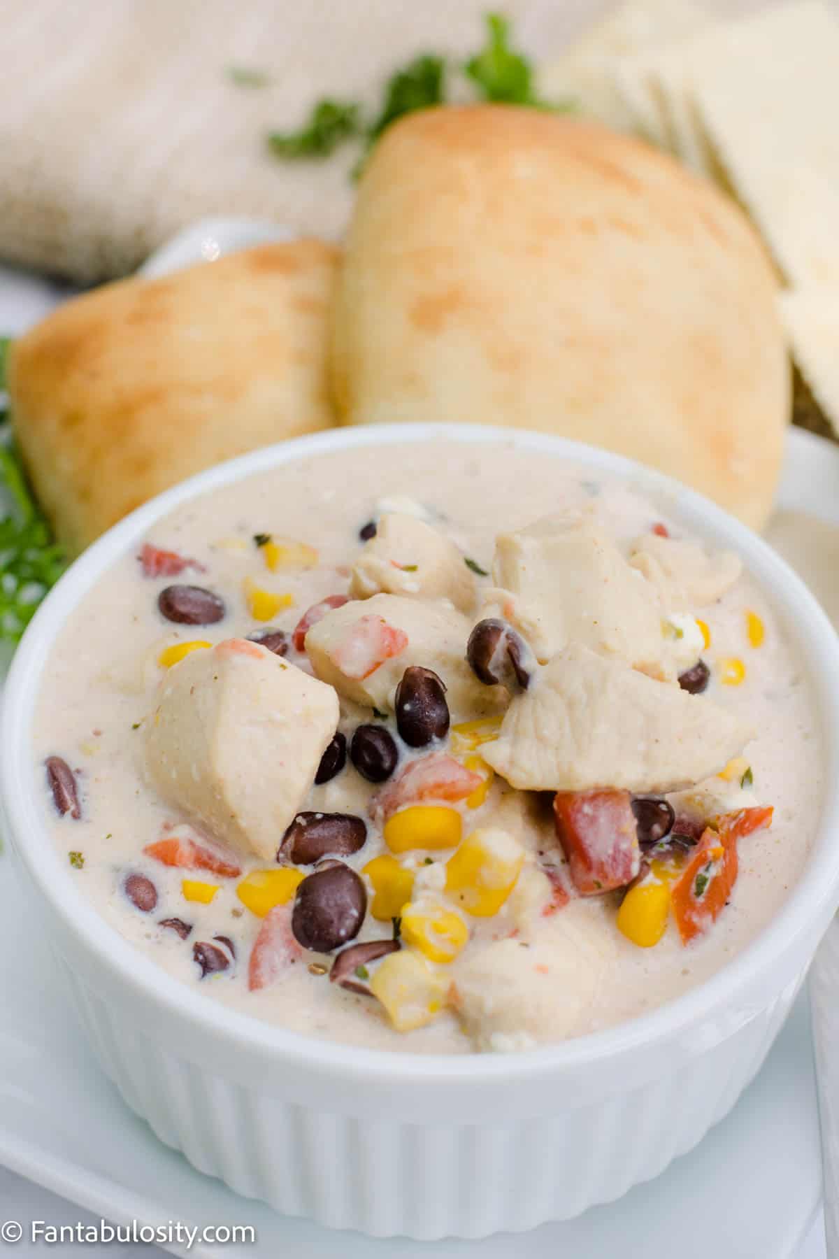 white chicken chili in bowl surround by rolls