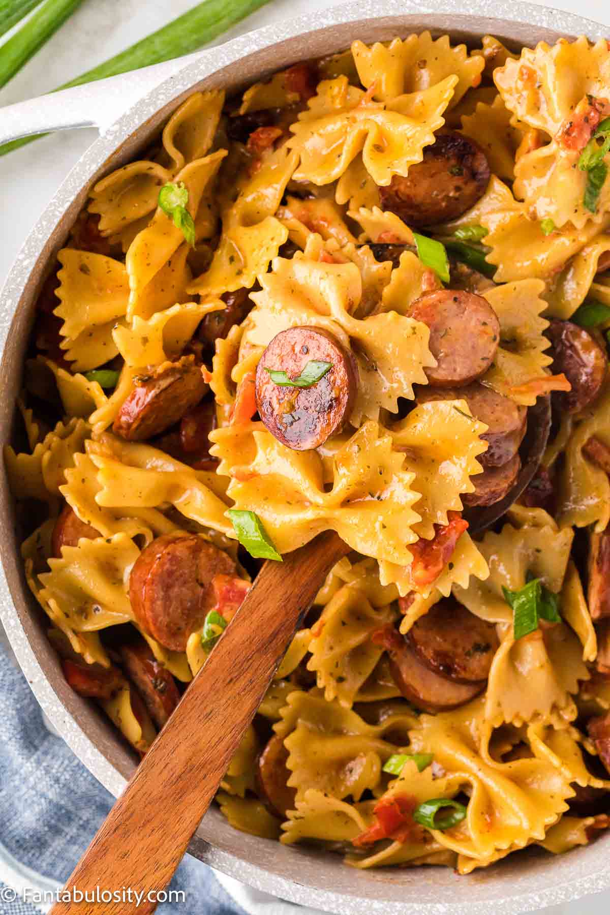 Close up of kielbasa pasta in pot, with a wooden spoon holding up a serving.