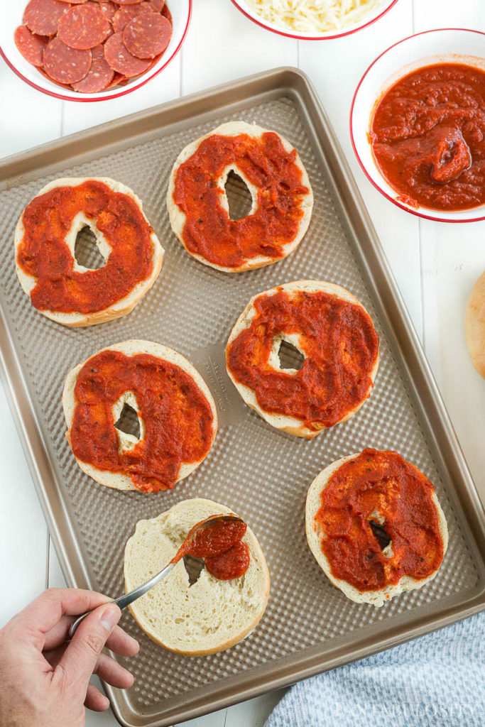pizza bagels with tomato sauce on a baking sheet
