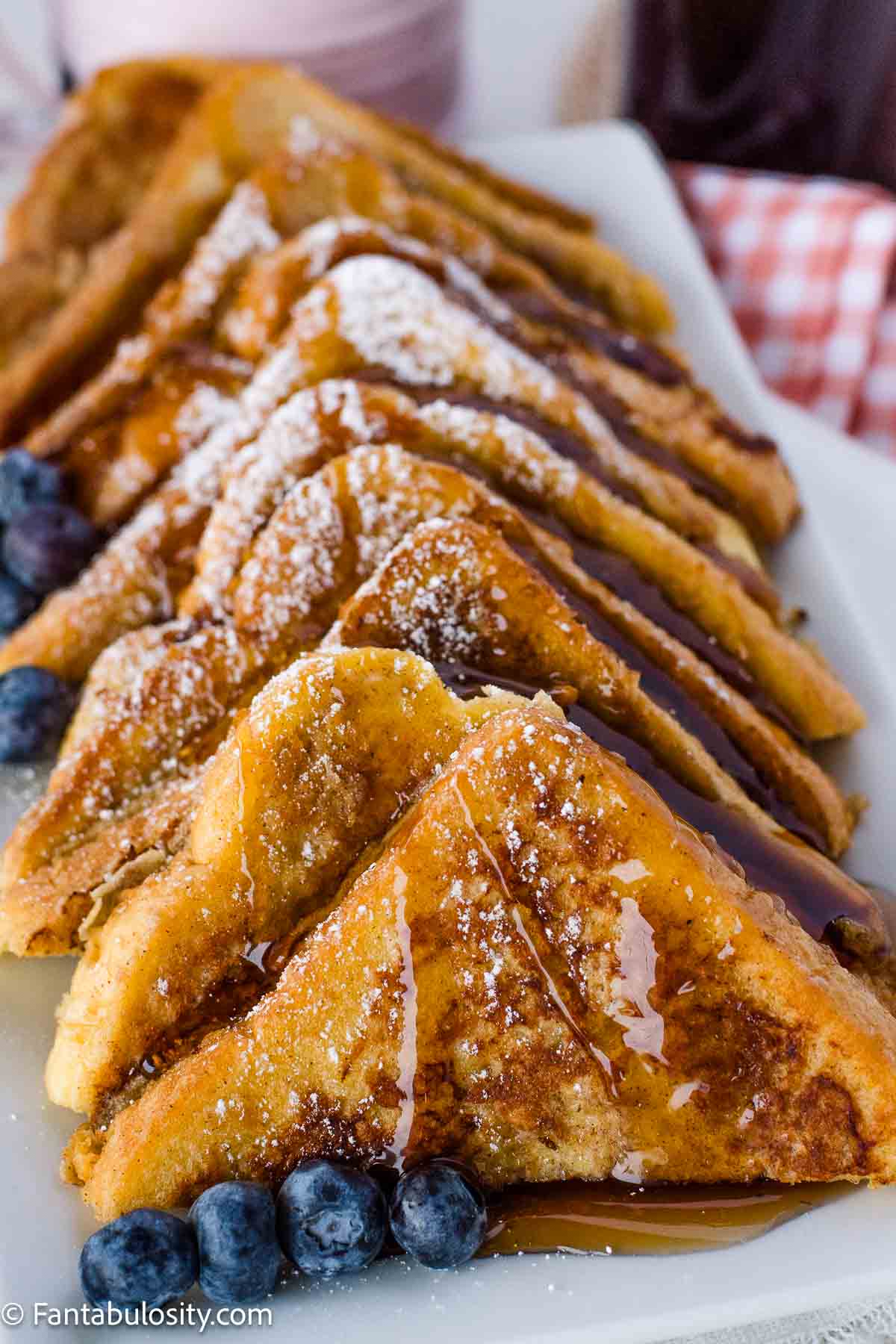 Slices of French toast on a platter, covered in syrup and powdered sugar.
