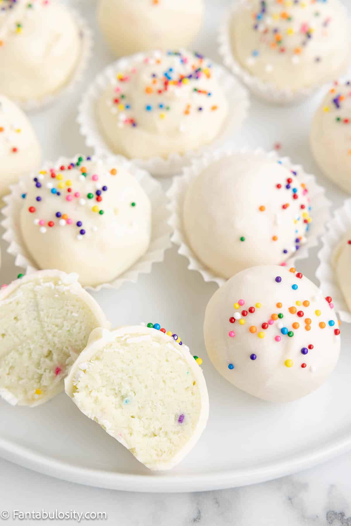 Showing the inside of a sugar cookie truffle on a white plate, sitting next to whole truffles.
