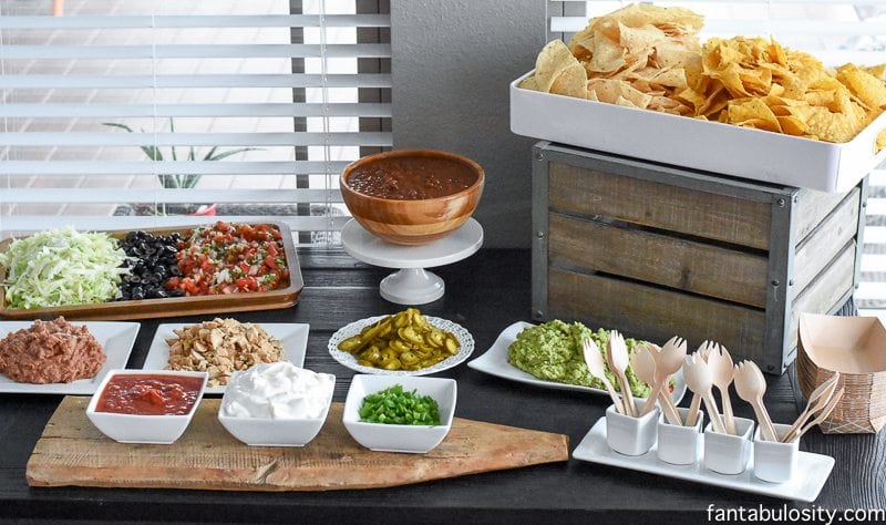 Table with nacho bar toppings in bowls and on plates