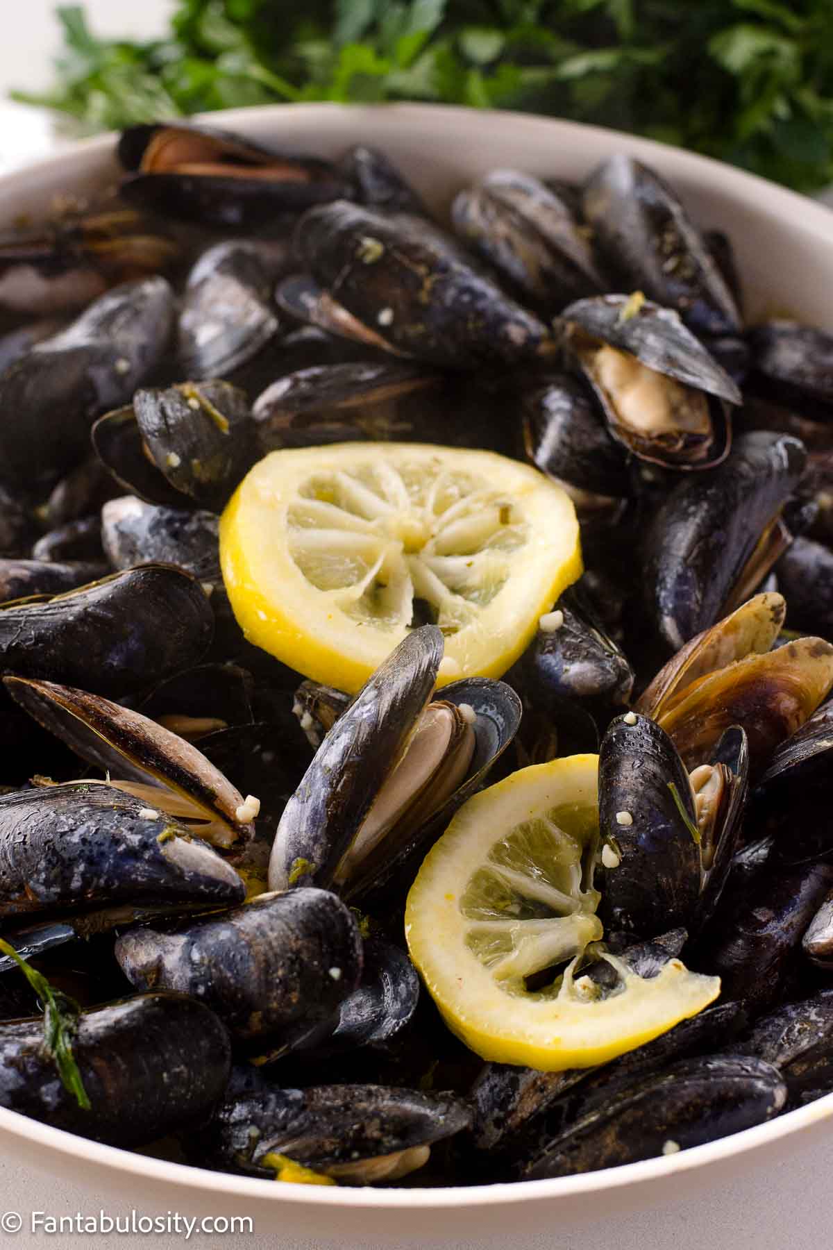 Steamed mussels in skillet with lemon slices on top.