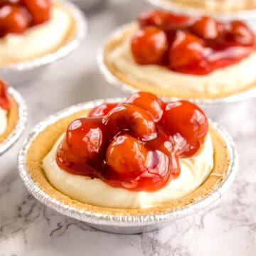 No bake mini cheesecakes on counter, with cherry pie filling on top.