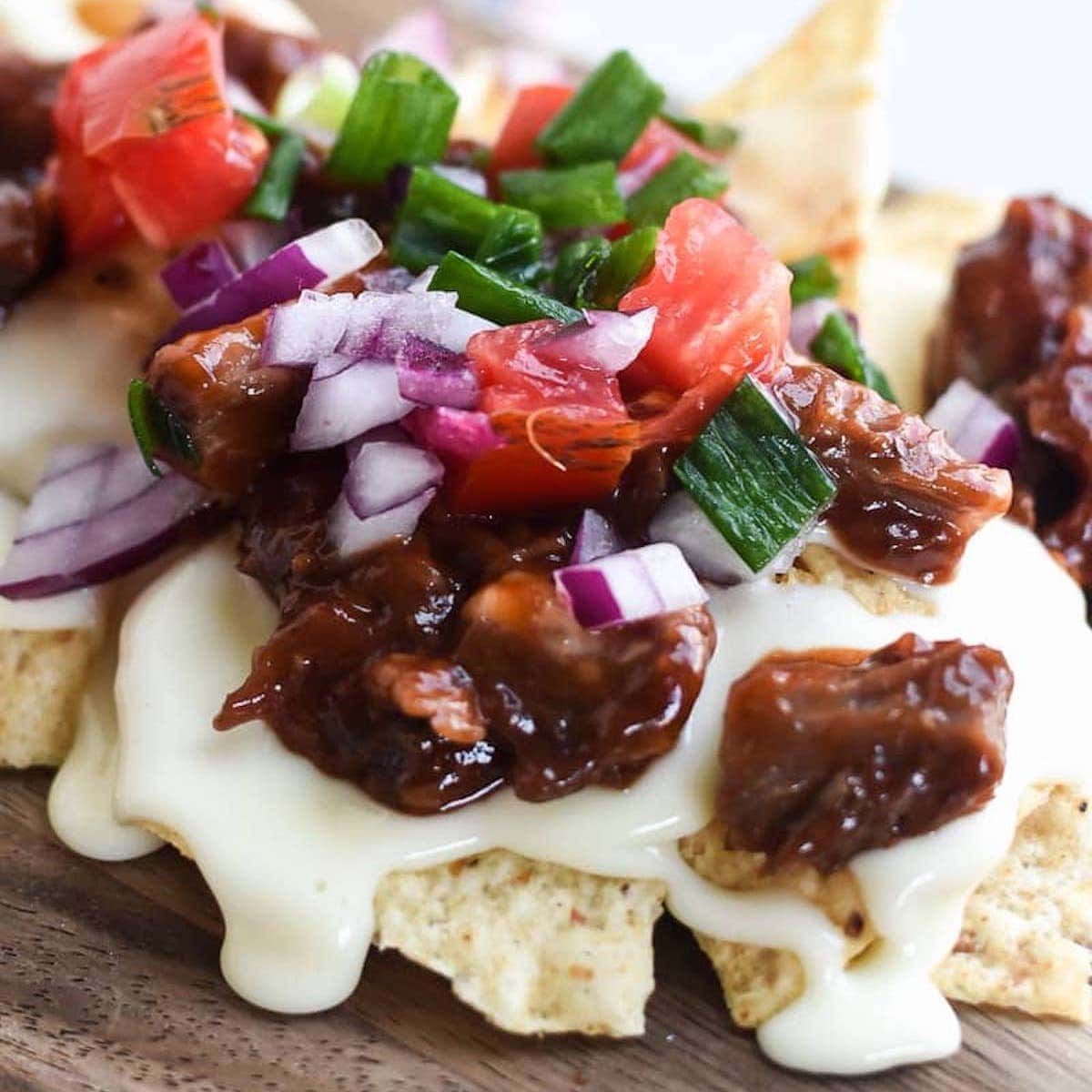 BBQ White Queso Nachos on wooden cutting board.