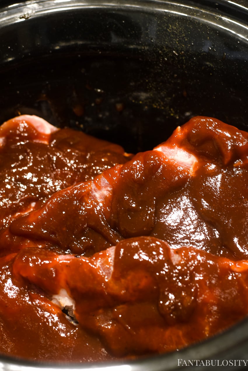 bbq sauce poured on top of raw pork steaks in slow cooker