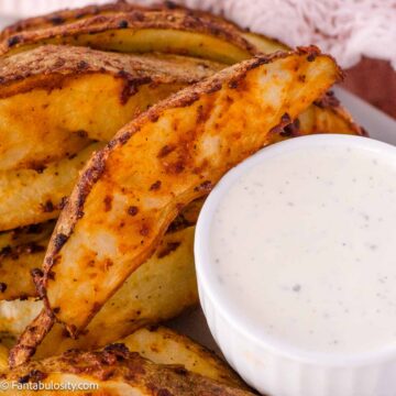 Fiesta Ranch potato wedges on plate next to a small bowl of ranch dressing.