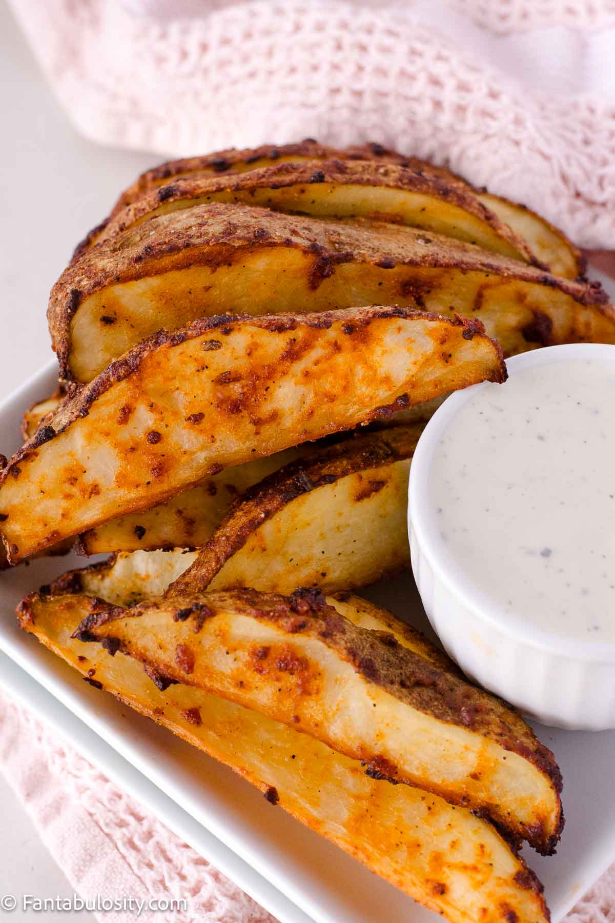 Baked potato wedges on a plate, sitting next to ranch dressing.