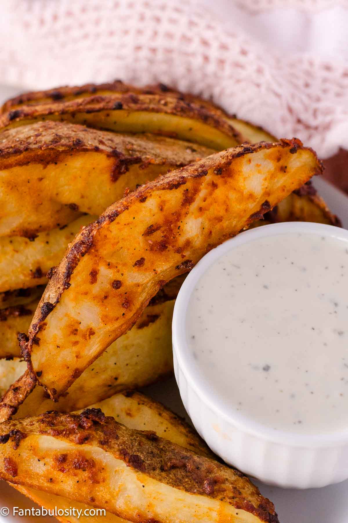 Fiesta ranch baked potato wedges on a plate, next to a small bowl of ranch dressing for dipping.