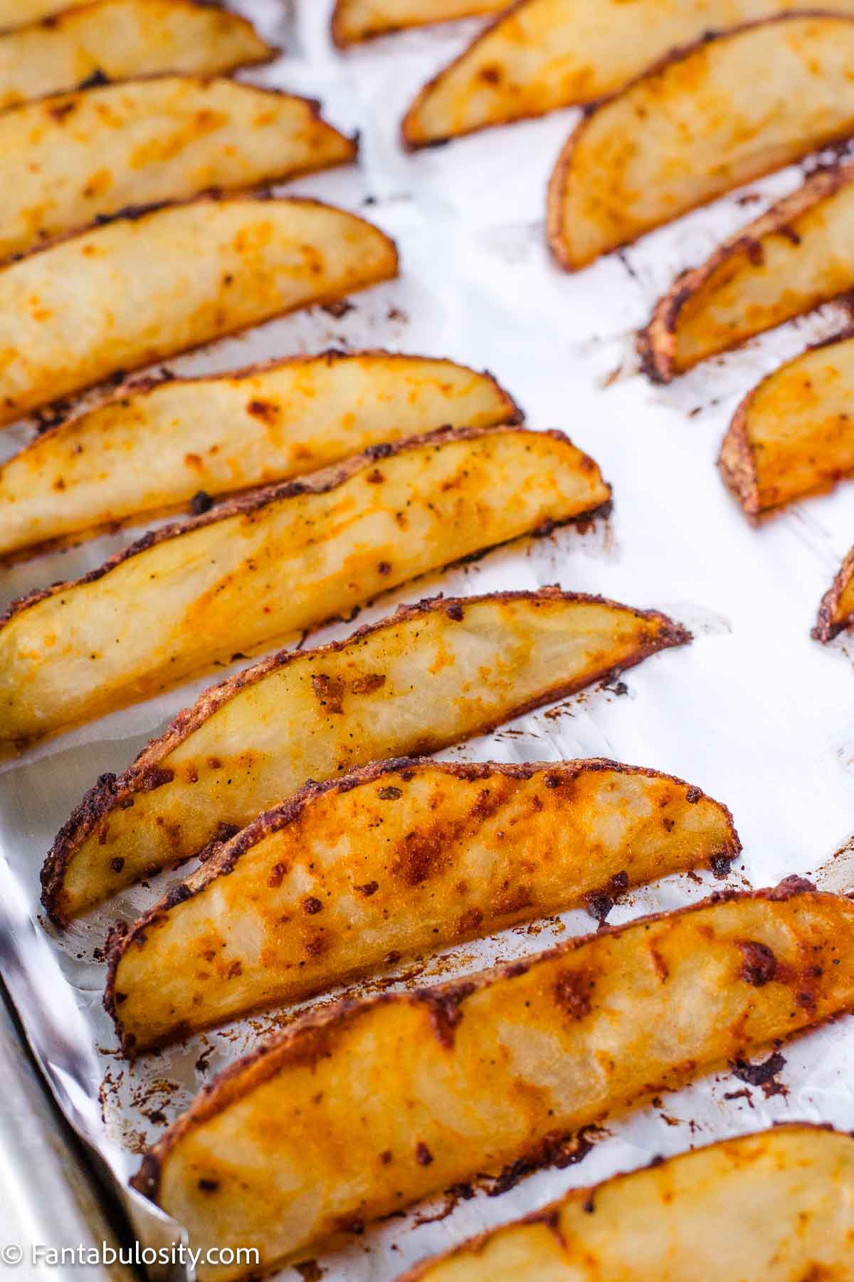 Baked potato wedges on baking sheet, that are seasoned with ranch seasoning.