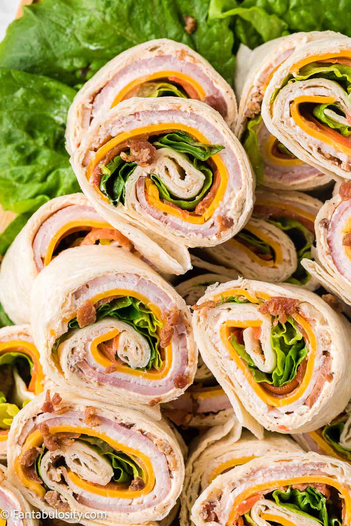 Pinwheel sandwiches stacked on top of one another, on cutting board.