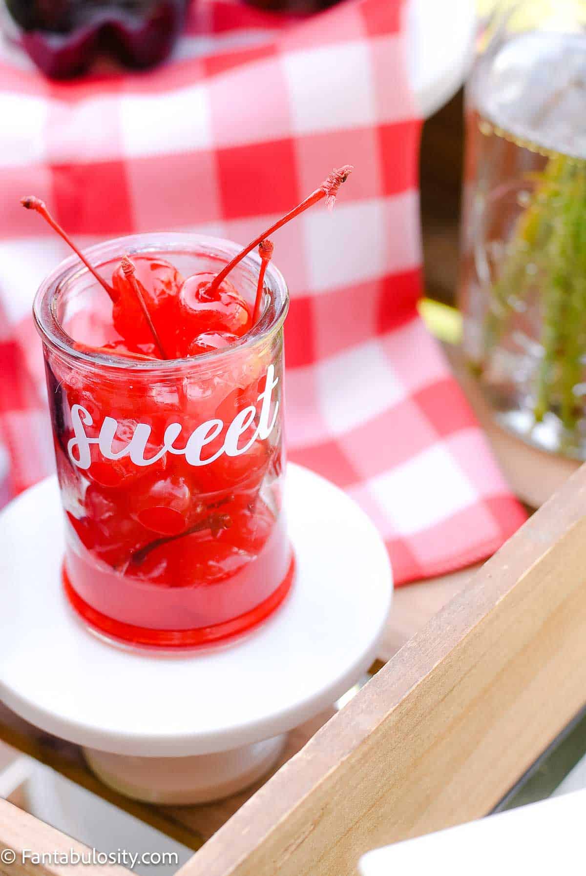 Cherries in small glass jar, sitting on drink station.