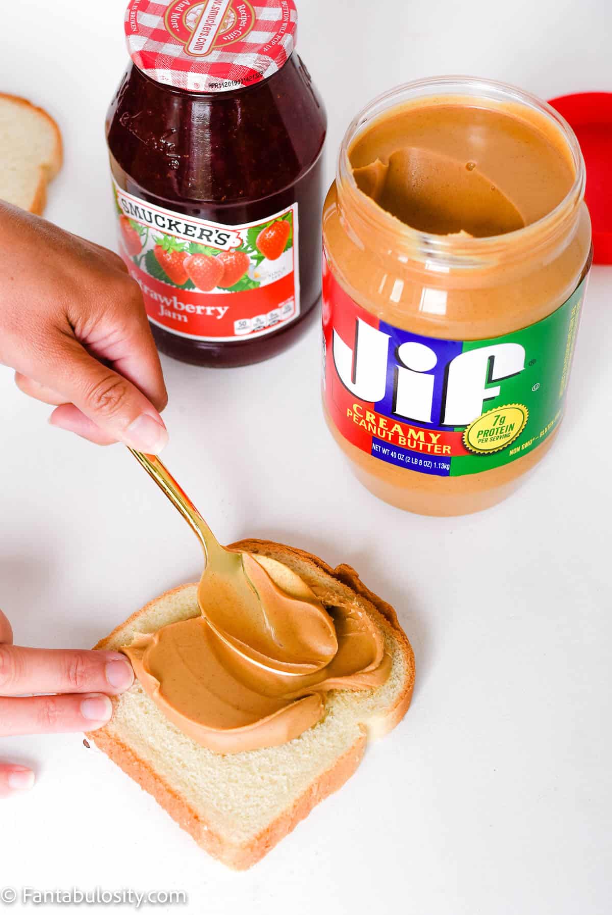 hand spreading peanut butter on bread with spoon