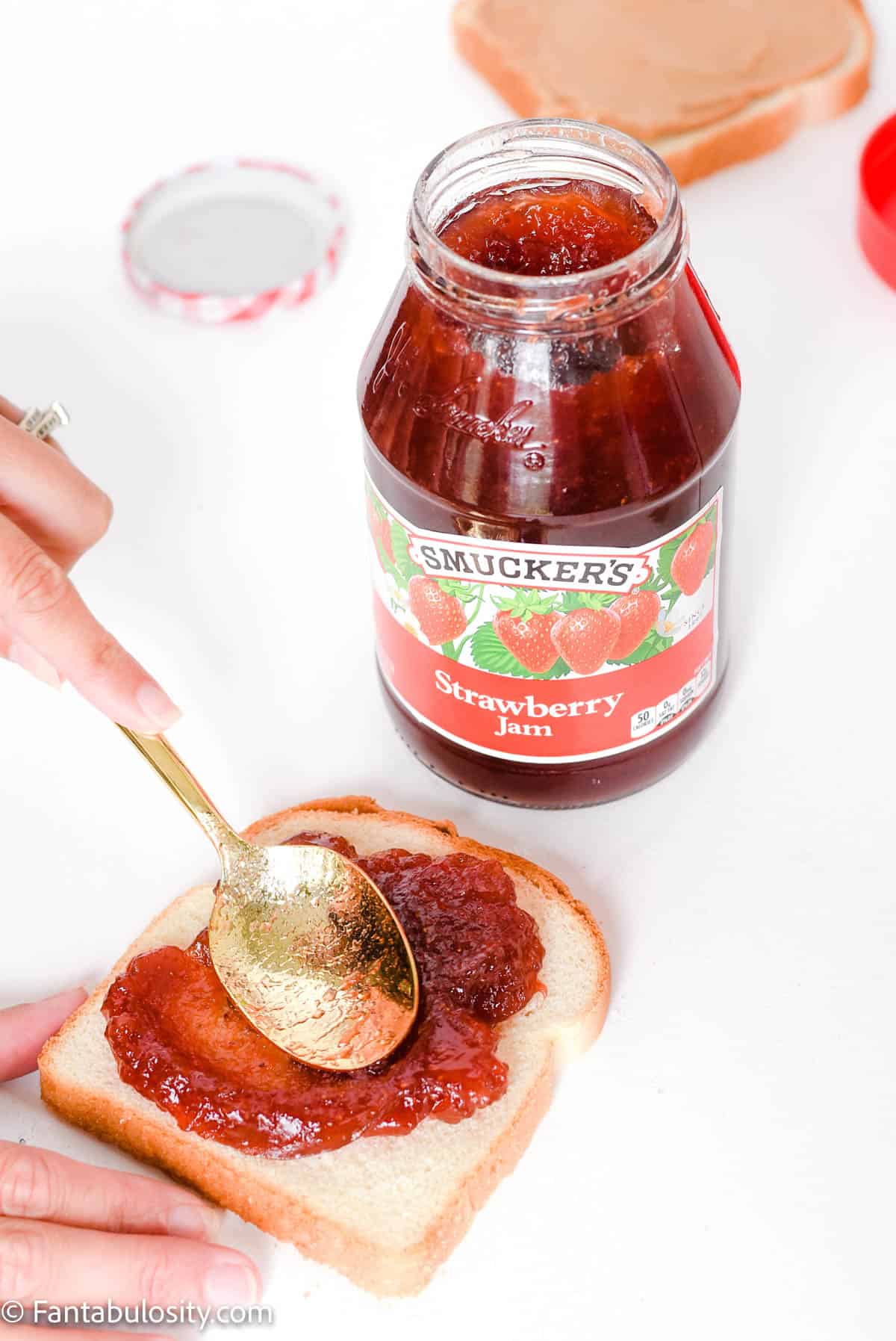 hand using spoon to spread jelly on bread