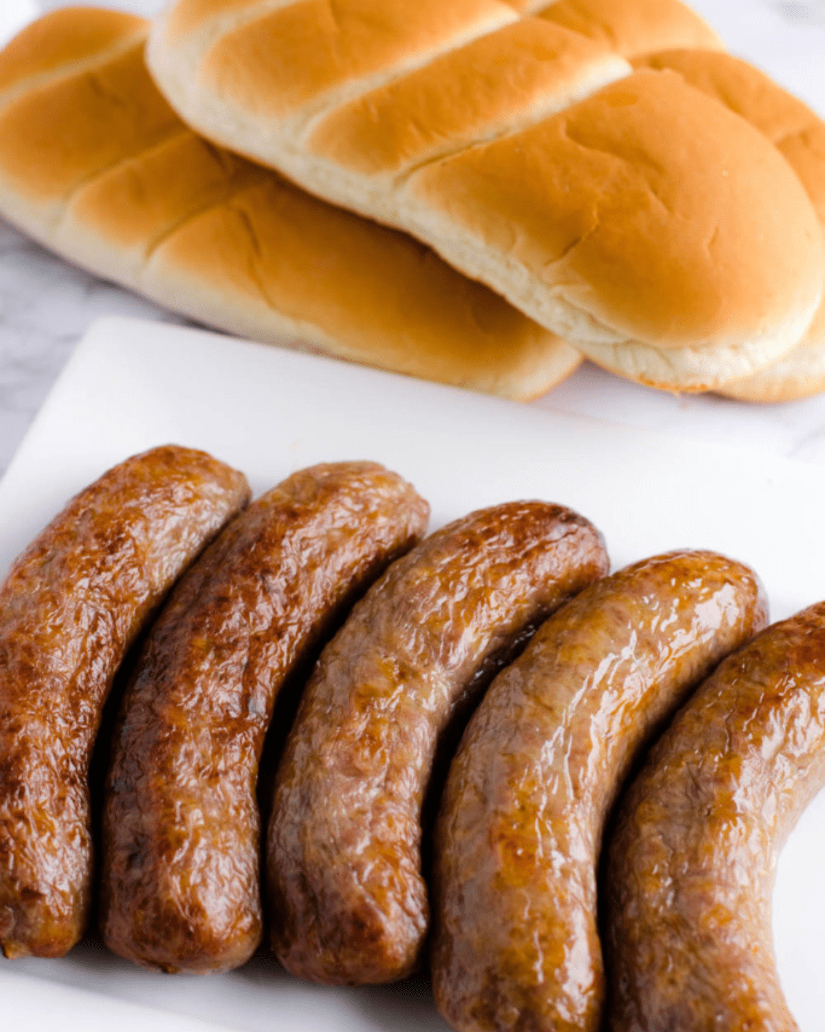 Air fryer brats on a white plate with buns