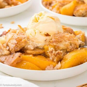 Bisquick Peach Cobbler serving on a. plate, with ice cream on top.