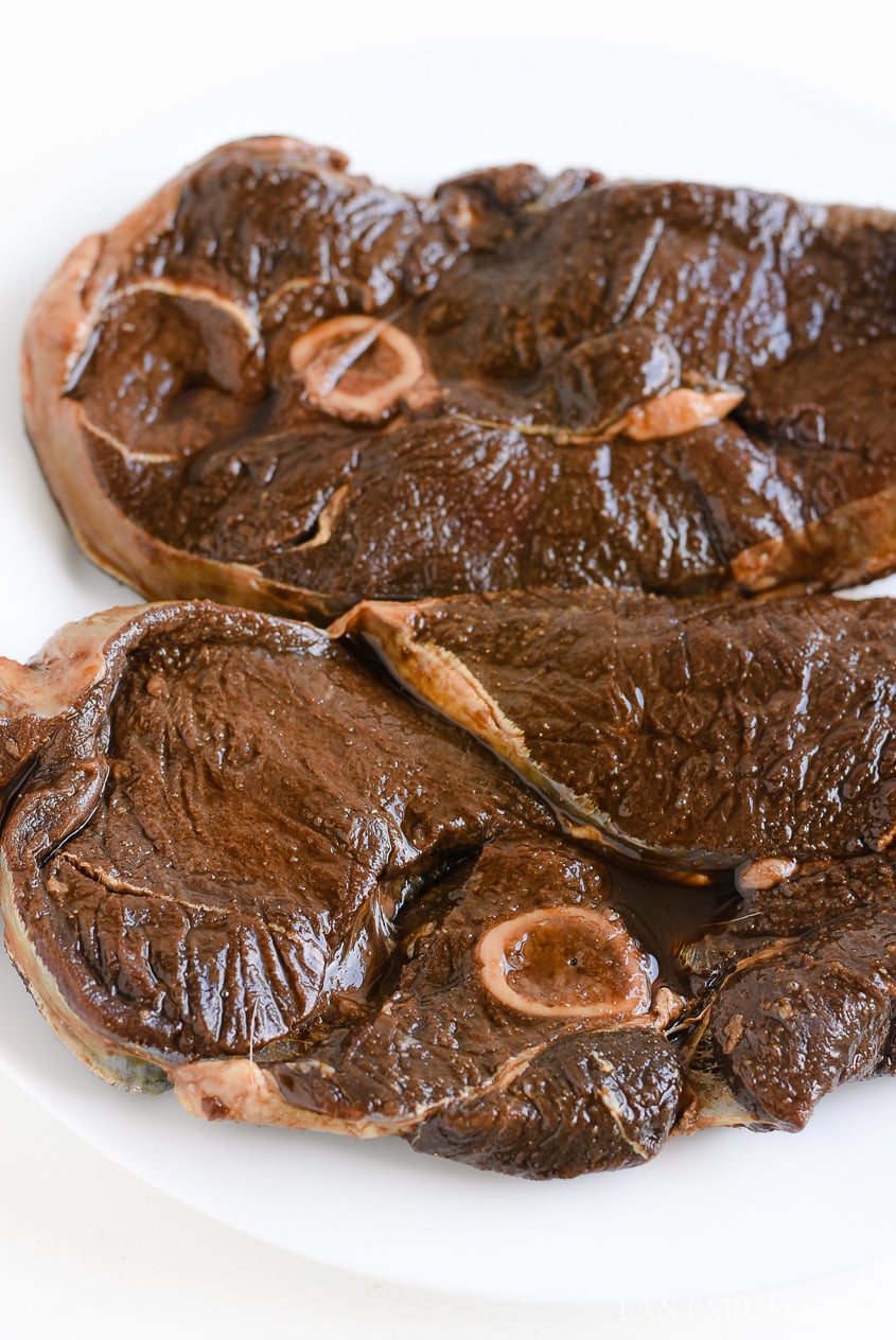 Deer steak sitting on white plate after marinating.