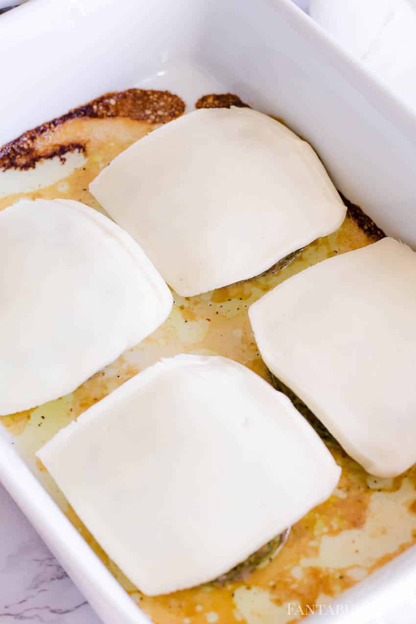 Sliced cheese on top of turkey burgers in baking dish