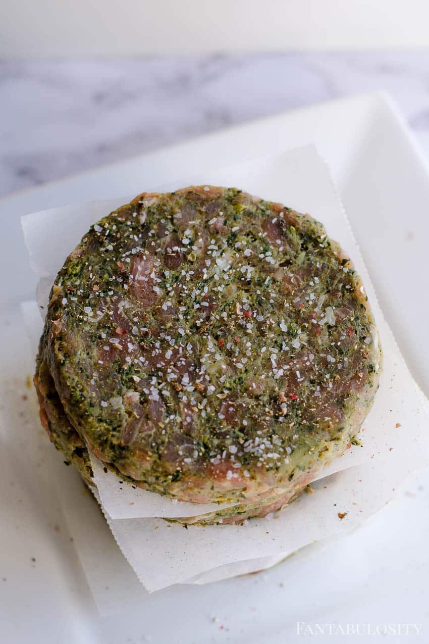 Seasoned burgers stacked on paper liners