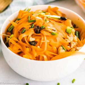 Carrot salad in small round bowl, by blue fabric napkin.