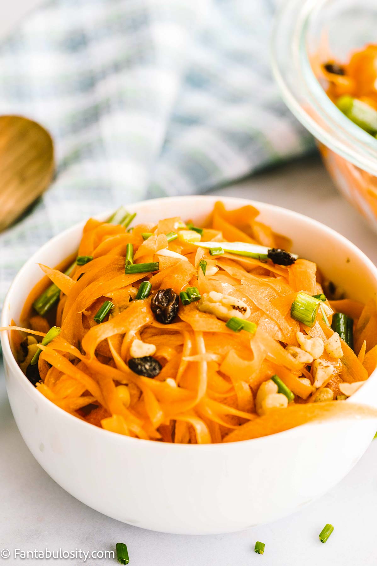 Carrot salad in round bowl, next to wooden spoon.