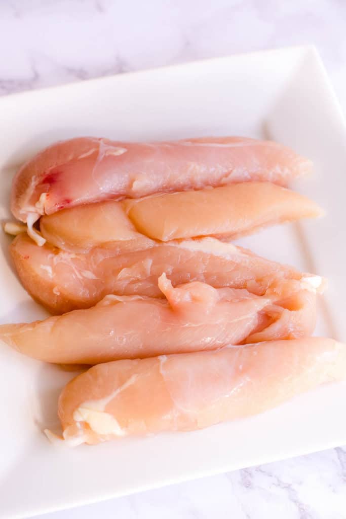 Raw chicken tenderloins on a white plate