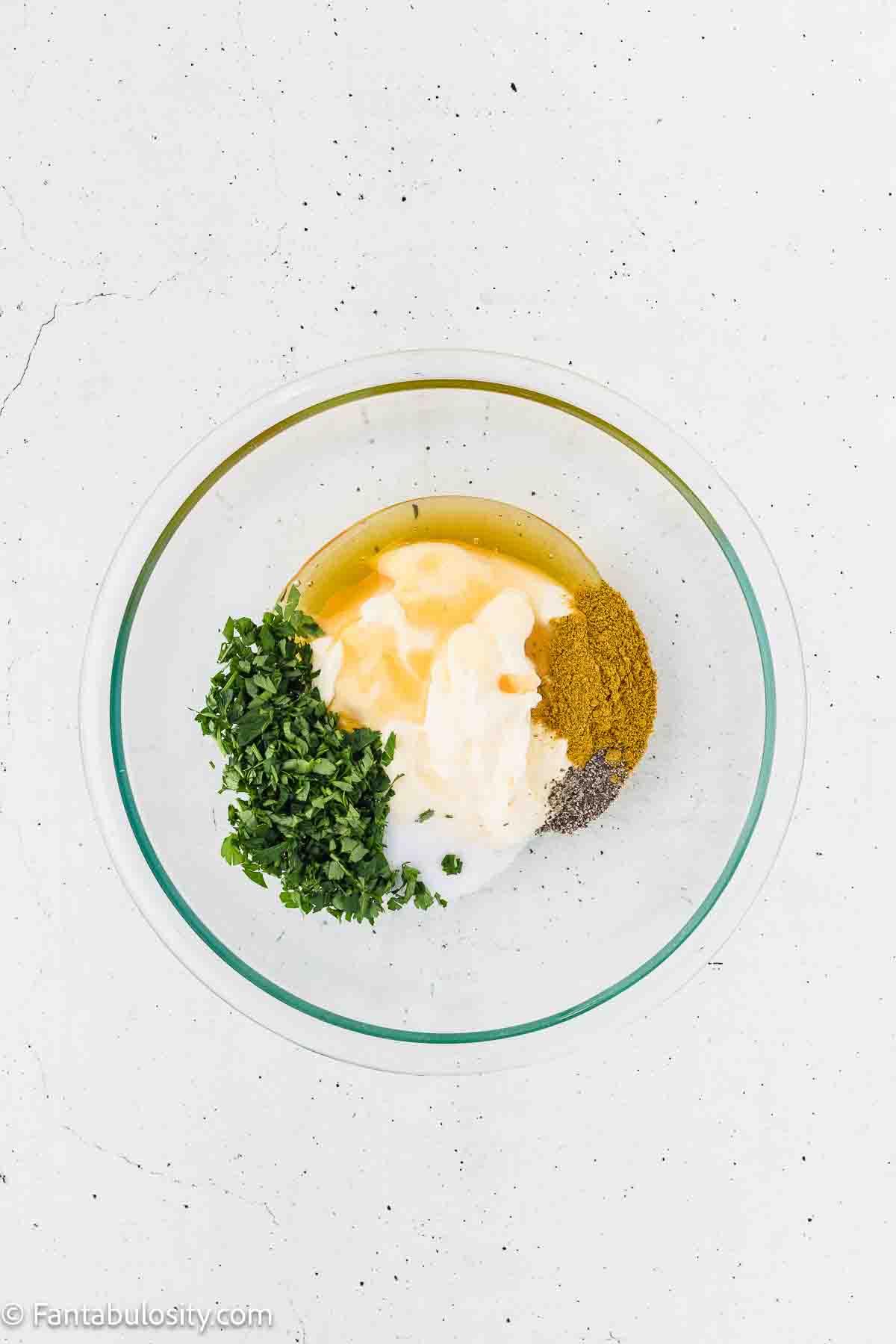 Mayo, curry, honey and fresh parsley in clear mixing bowl.
