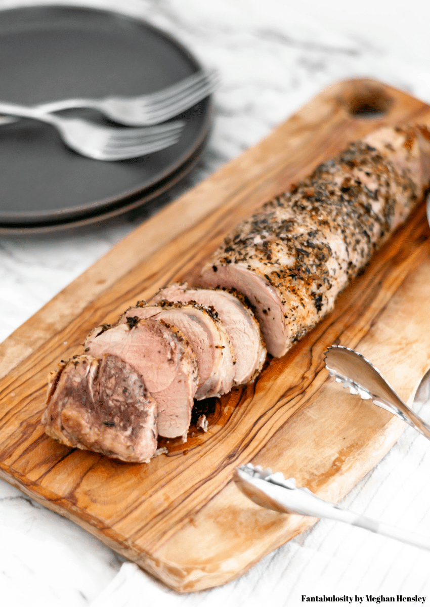 Roasted pork tenderloin cut in to slices on a wooden cutting board.