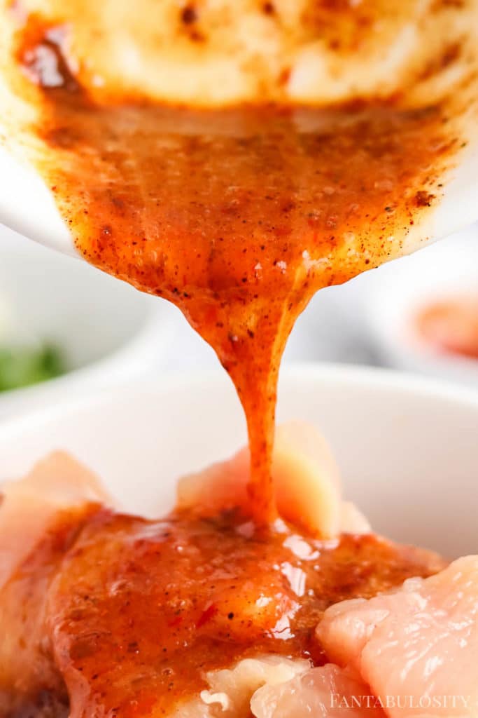 Chilli Chicken Sauce pouring over raw chicken in a bowl