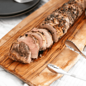 Roasted pork loin, sliced, on wood cutting board.