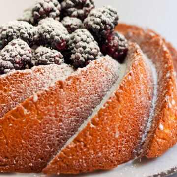 Pound cake made in a bundt pan, with powdered sugar and blackberries on top.