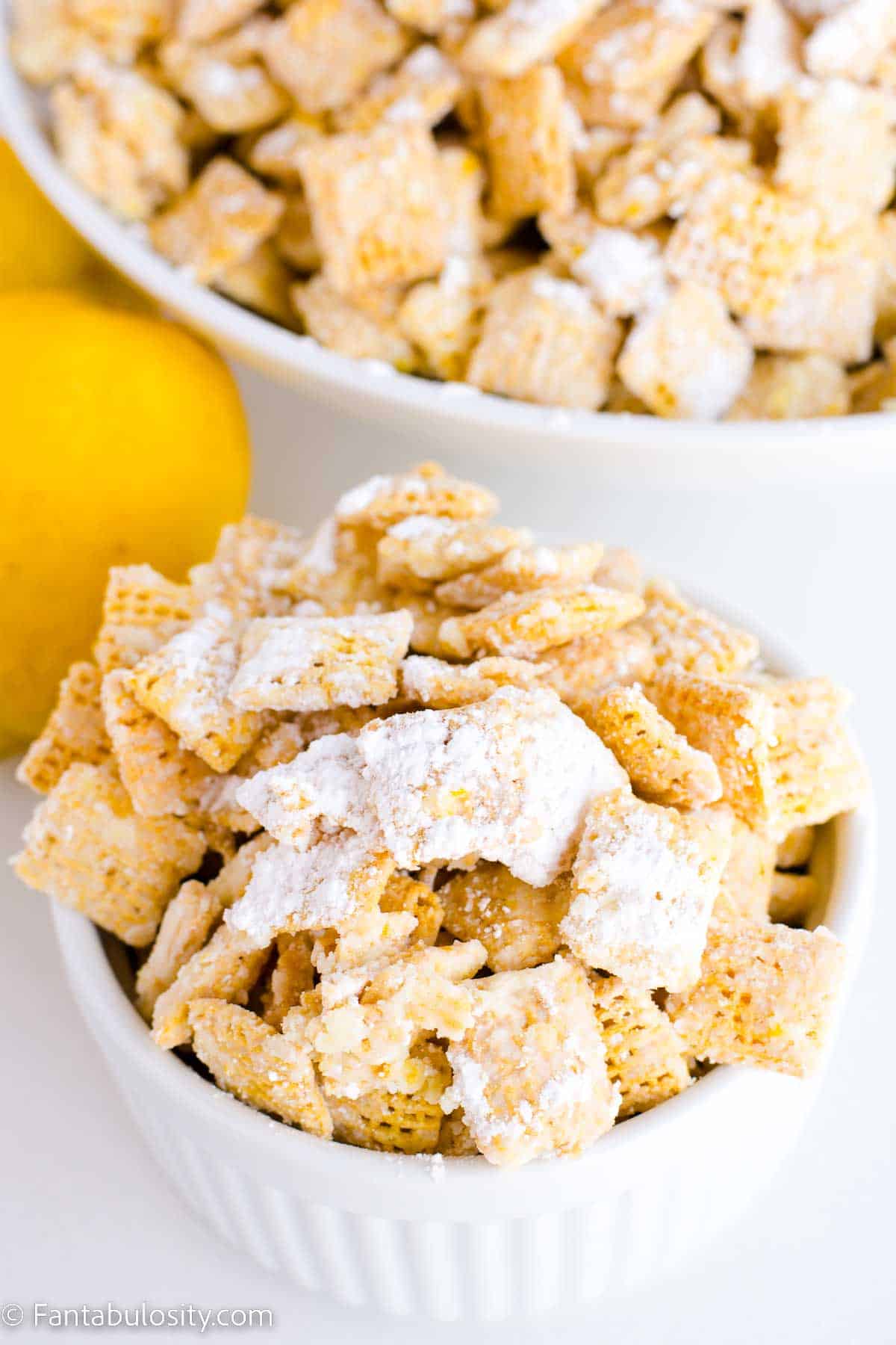 Lemon puppy chow in white bowl, sitting next to lemons.