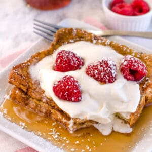Brioche French Toast slices on white plate with cream and berries
