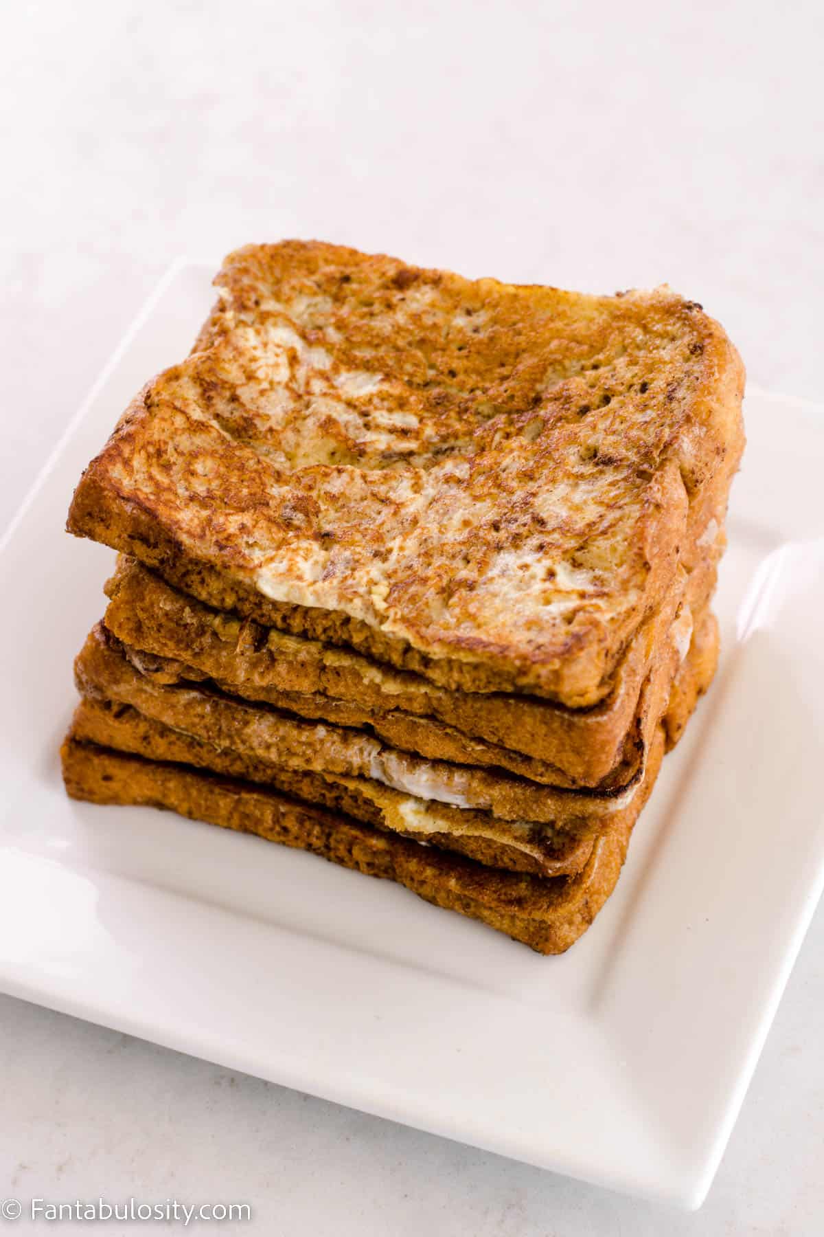 Cooked french toast stacked on white plate