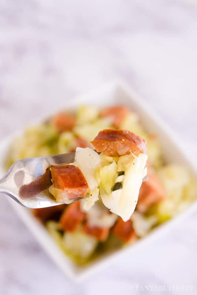 Kielbasa and Cabbage in a white bowl, on a fork