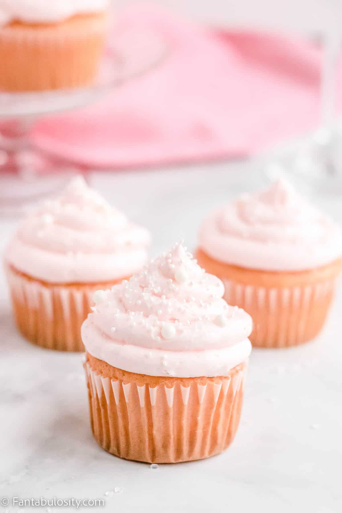Pink champagne cupcakes on marble counter.