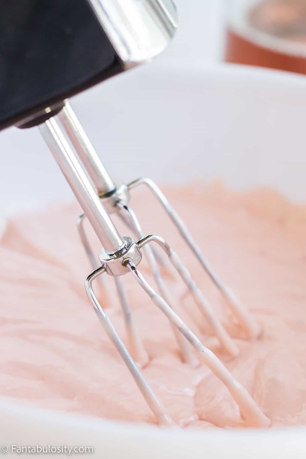 Hand mixer mixing cupcakes in mixing bowl.