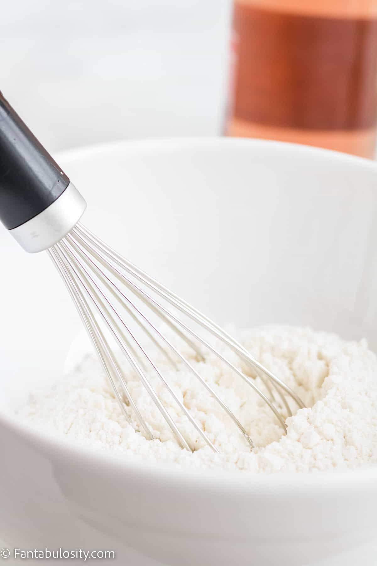 Flour and dry ingredients in white bowl with whisk.