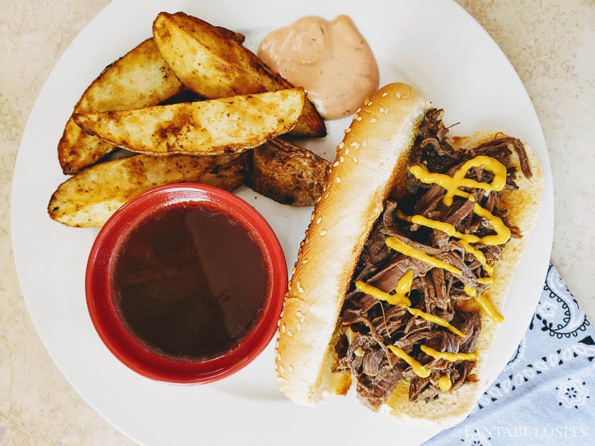 French Dip Sandwiches on a white plate with potato wedges and sauce