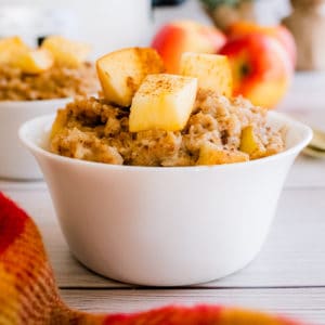 apple cinnamon oatmeal in a small white bowl with apple pieces on top