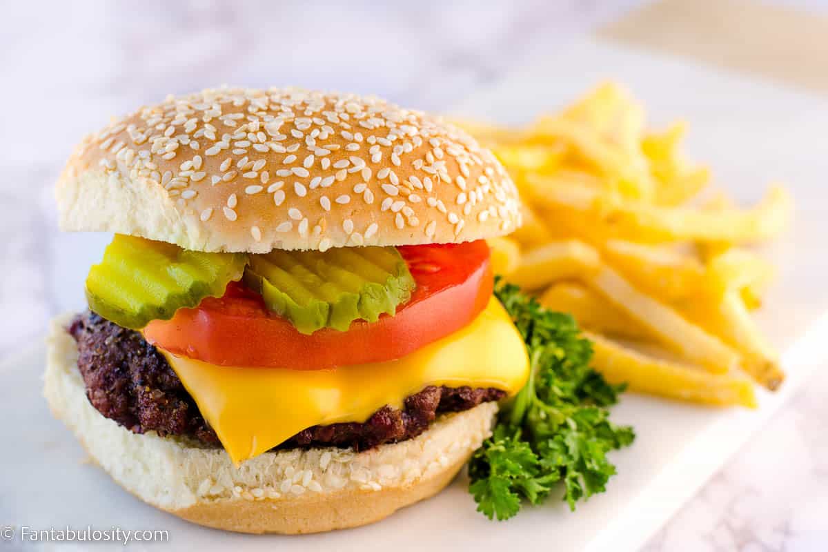 Smoked burger on white plate, next to french fries.