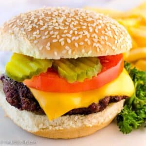 Smoked burger on a white plate, topped with pickles, cheese and tomato.