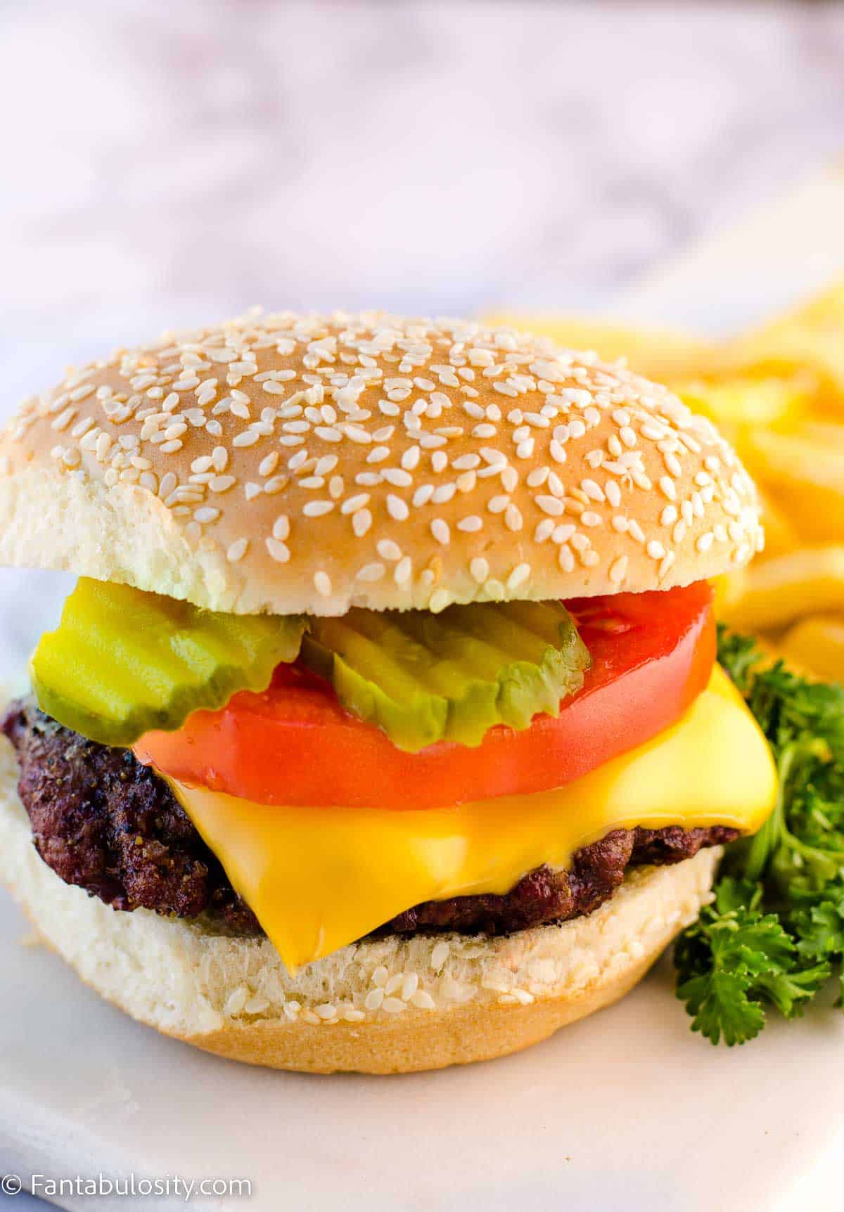 Smoked burger on white plate, topped with pickles, tomato, and cheese.