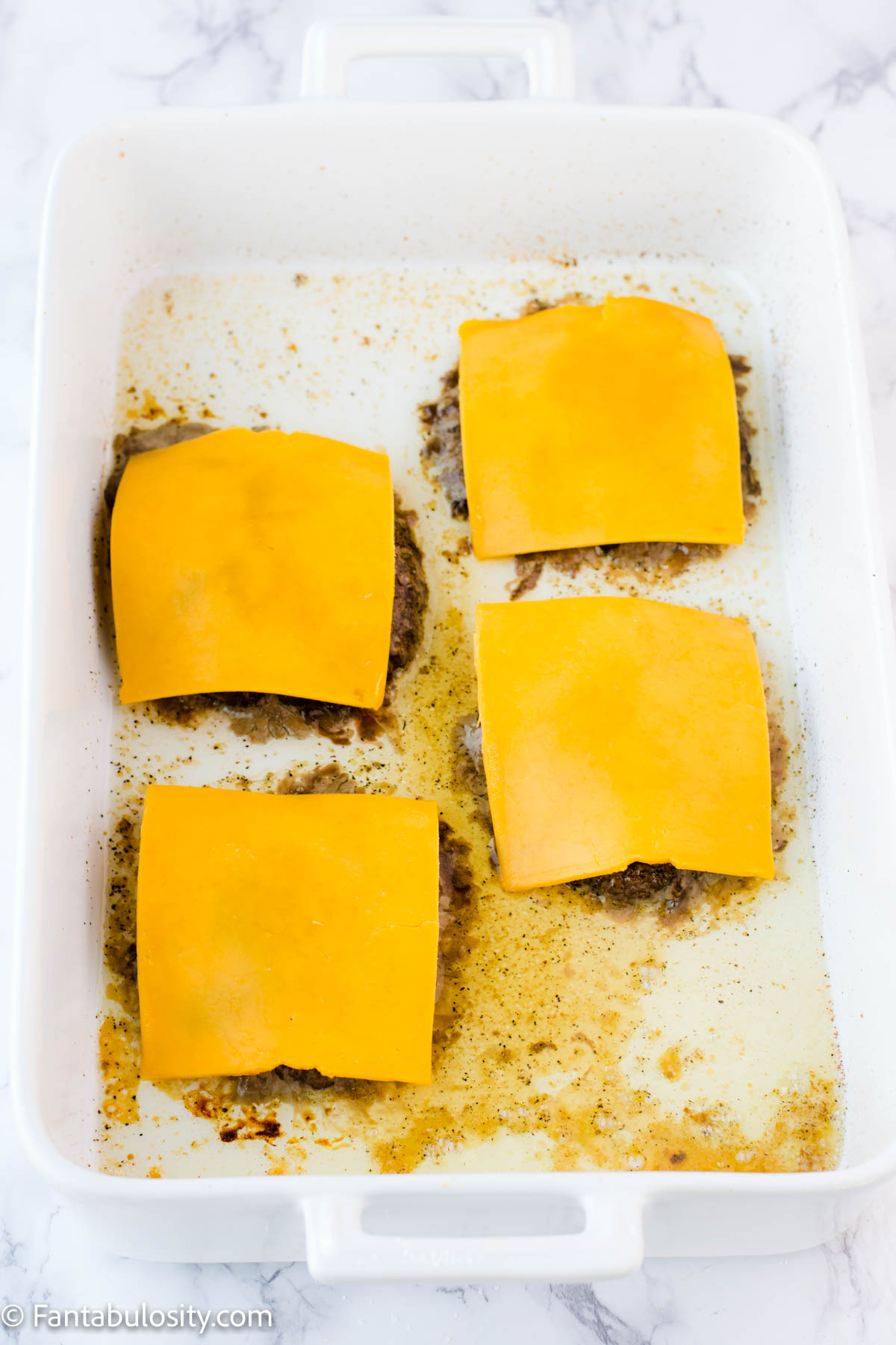 Baked burger patties in baking dish with cheese slices on top.