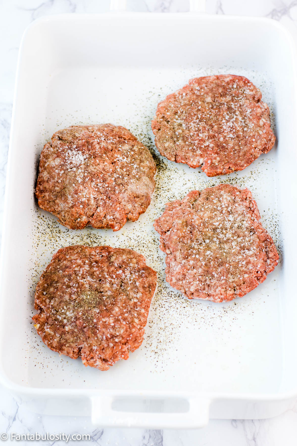 Seasoned frozen burger patties in baking dish.