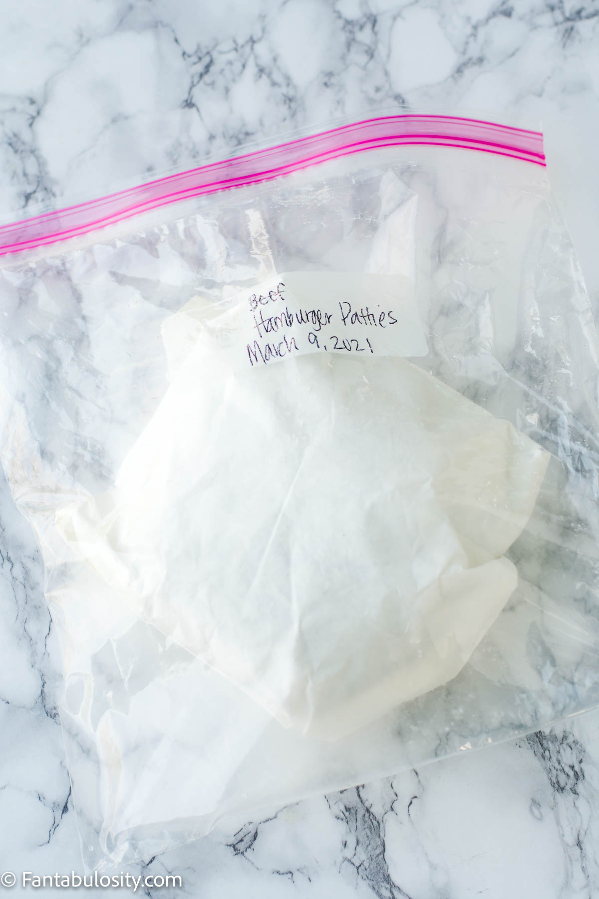 Frozen burger patties in wax paper placed in a ziploc bag.